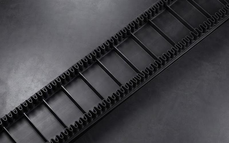 Black belt with corrugated sidewalls and transverse cleats, seen diagonally on a grey background